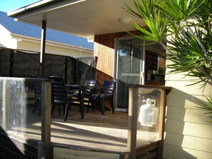 Un patio techado al aire libre con una mesa, sillas, cerramiento de vidrio y una planta en maceta.