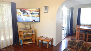 A living room with a television, wooden furniture, and a view to the dining area. - Manly Peninsular (Wynnum)