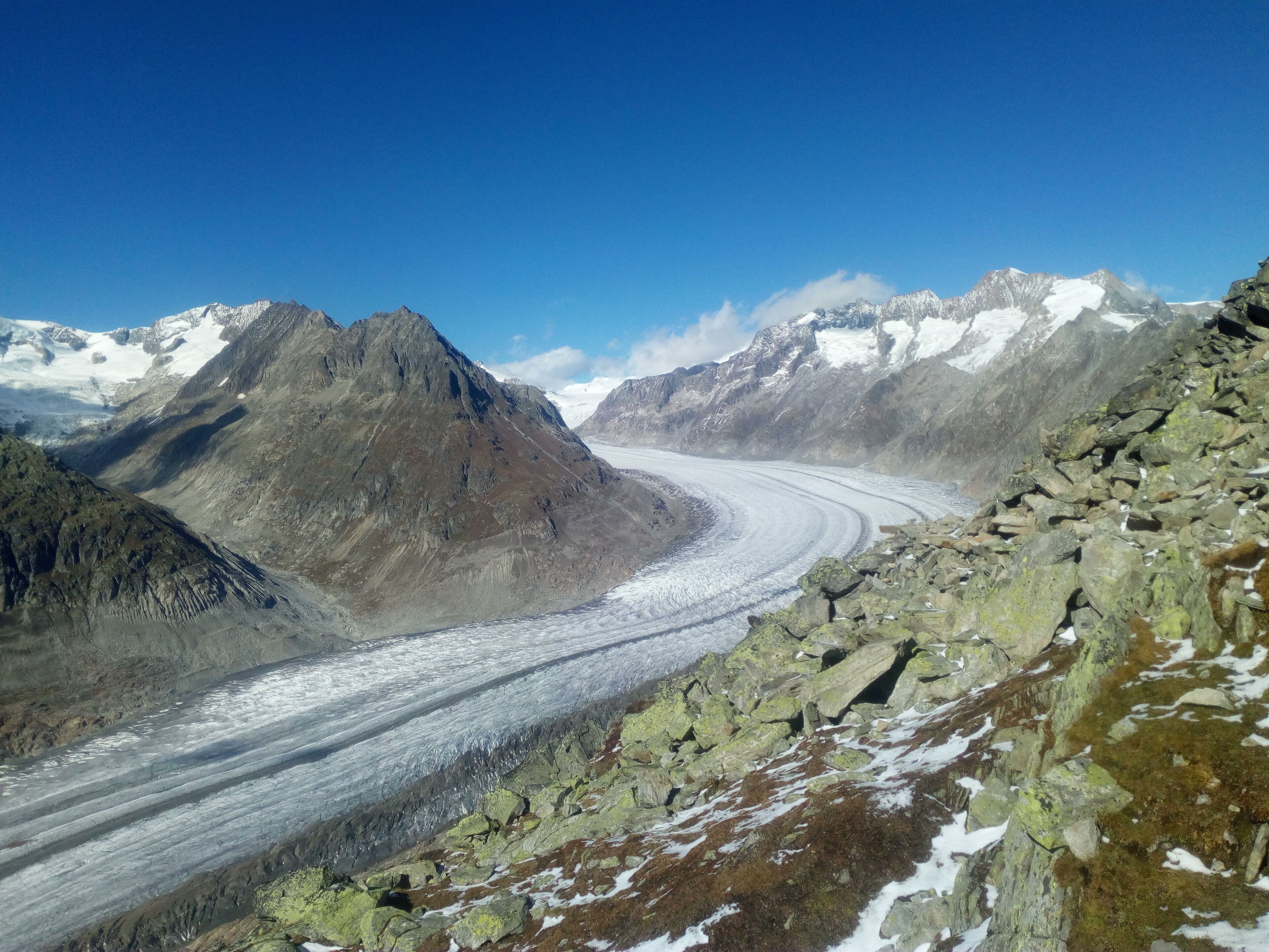 A glacier winding through a mountainous landscape with rocky terrain and snow-capped peaks.