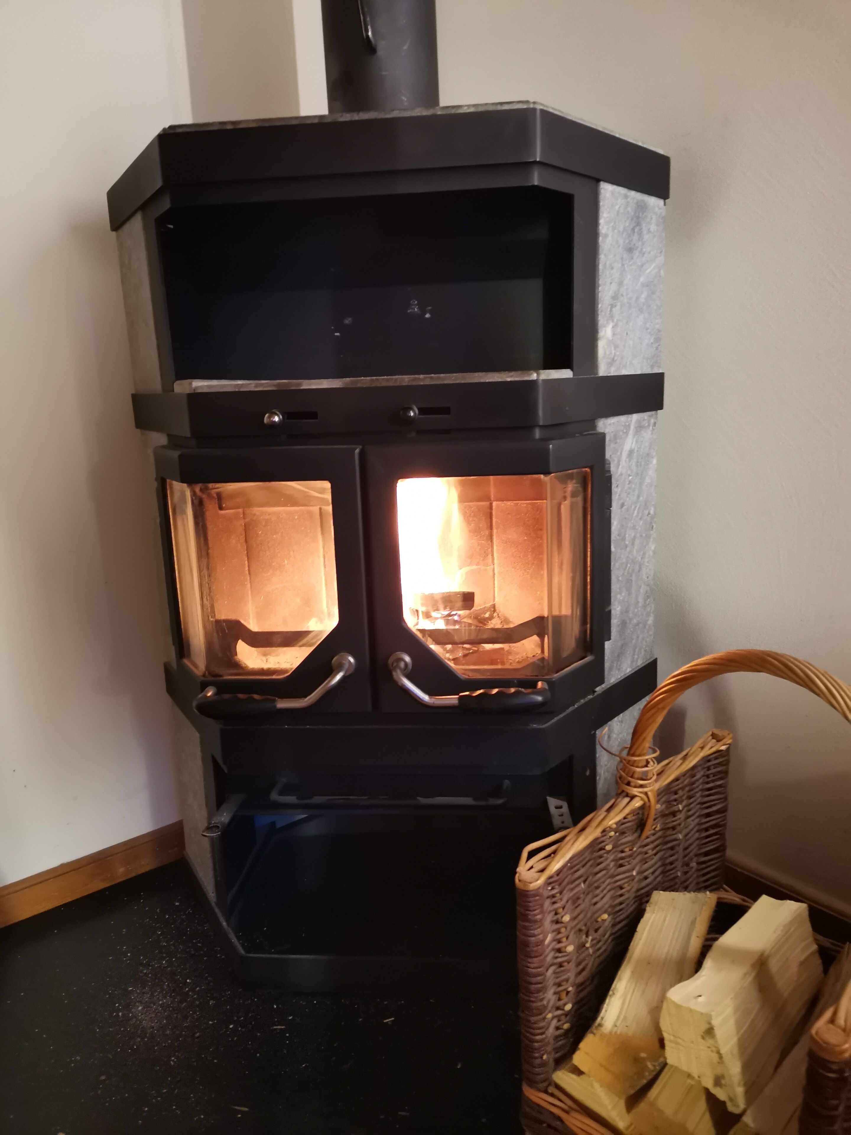 En brændeovn med to glasdøre, en kurv med brænde og et vægmonteret kontrolpanel.