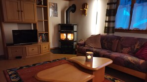 Un salon chaleureux avec un téléviseur, des meubles en bois, un canapé, un tapis à motifs et un poêle à bois.