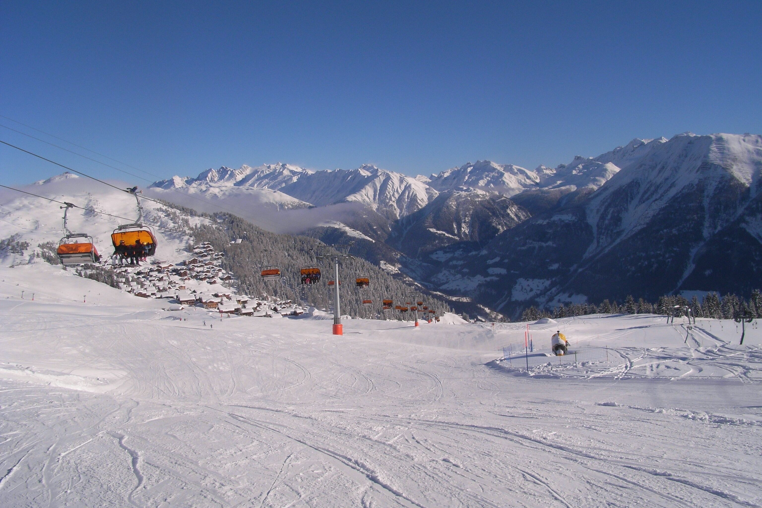 Une piste de ski avec un télésiège, des montagnes enneigées et un ciel dégagé.