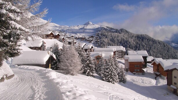 Un village de montagne enneigé, avec des maisons en bois et une piste de ski.
