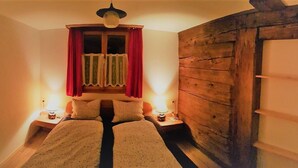 Une chambre avec deux lits, une armoire en bois, une fenêtre avec des rideaux et des lampes de chevet.