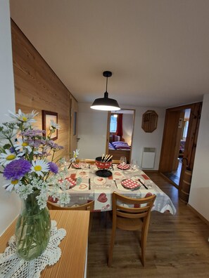 A dining area with a wooden table set for two, a vase of flowers, and a hanging light fixture. - Cozy family-friendly apartment in an idyllic hamlet (Grengiols)