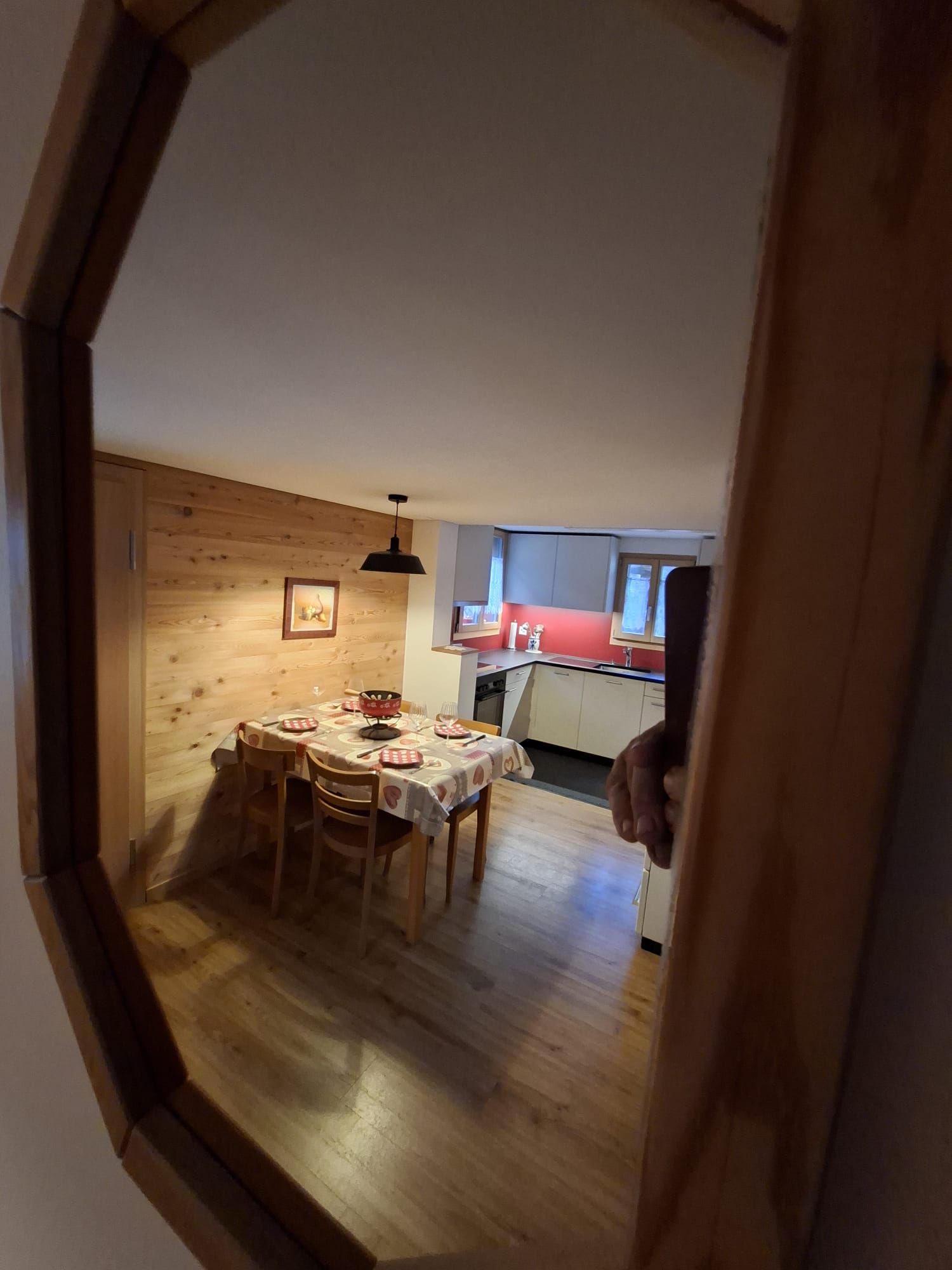 En spiseplads med et bord dækket til fire personer, trævægge og et køkken i baggrunden.