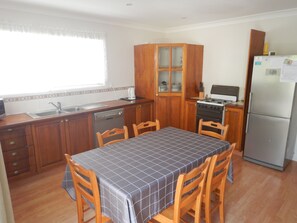 A compact kitchen with wooden cabinets, a gas stove, a refrigerator, and a dining table with chairs.