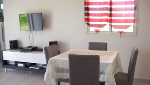 A dining area with a table set for four, a television mounted on the wall, and a window with red and white curtains.