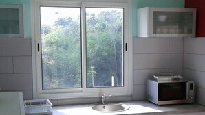 A kitchen with white cabinets, a double sink, a microwave, and a window with a view of greenery.
