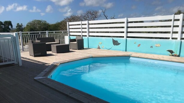 A swimming pool with a wooden deck, a white fence, and outdoor seating.