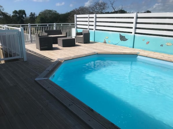 A swimming pool with a wooden deck, a white fence, and a mural with marine life.