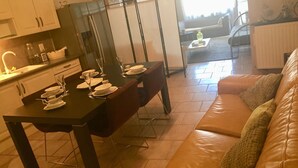 Un comedor con una mesa dispuesta para cuatro personas, un sofá y una cocina al fondo.