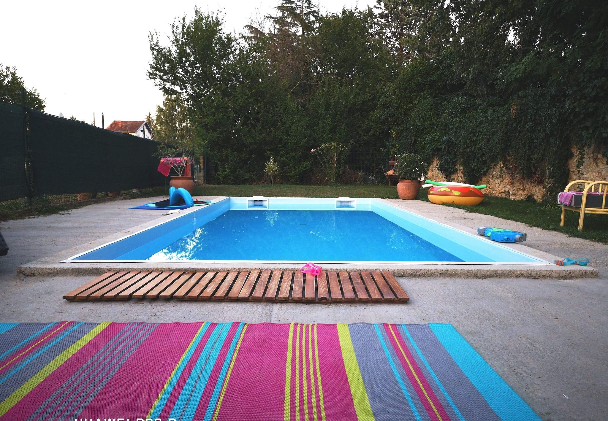 Piscina com deck de madeira e tapetes coloridos.