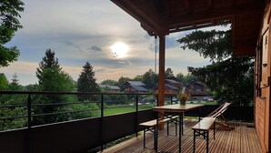 A wooden deck with a table and benches, overlooking a grassy area and houses.