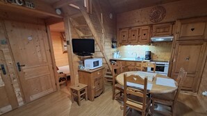A wooden cabin interior with a dining table, chairs, a television, a microwave, and a kitchenette.