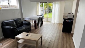 A living room with a black leather sofa, a wooden coffee table, and a dining area with a table and chairs. - Cedar Lookout (Wynnum)