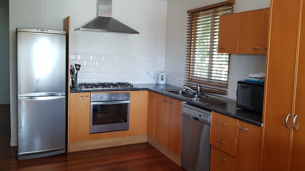 A kitchen with wooden cabinets, stainless steel appliances, a dishwasher, and a window with blinds. - Cedar Lookout (Wynnum)