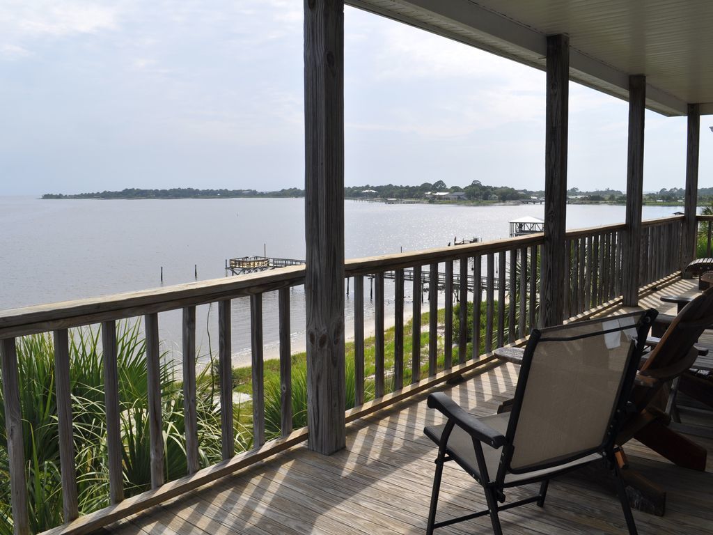 A covered outdoor area with a view of a lake, a dock, and a chair.