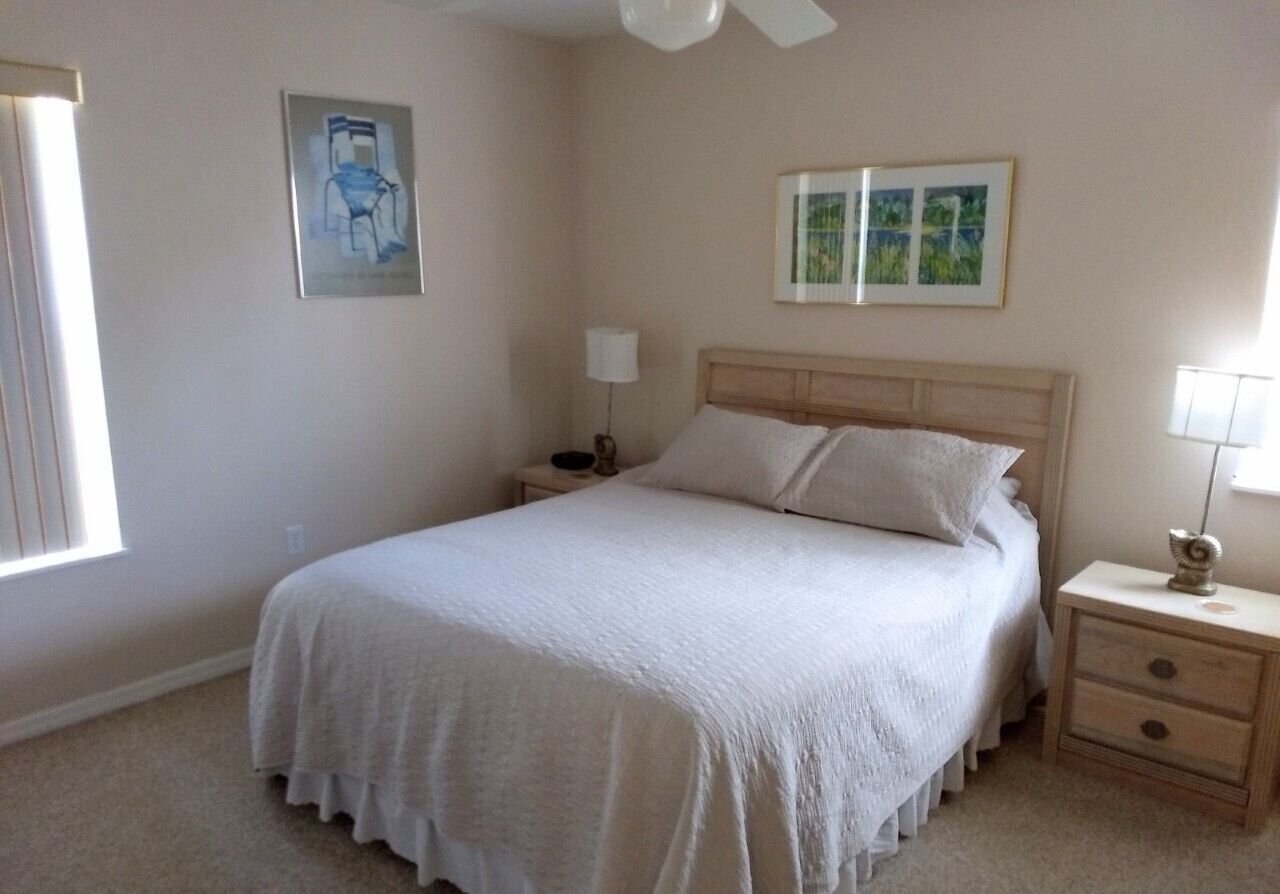 A bedroom with a bed, nightstands, a ceiling fan, and artwork on the walls.