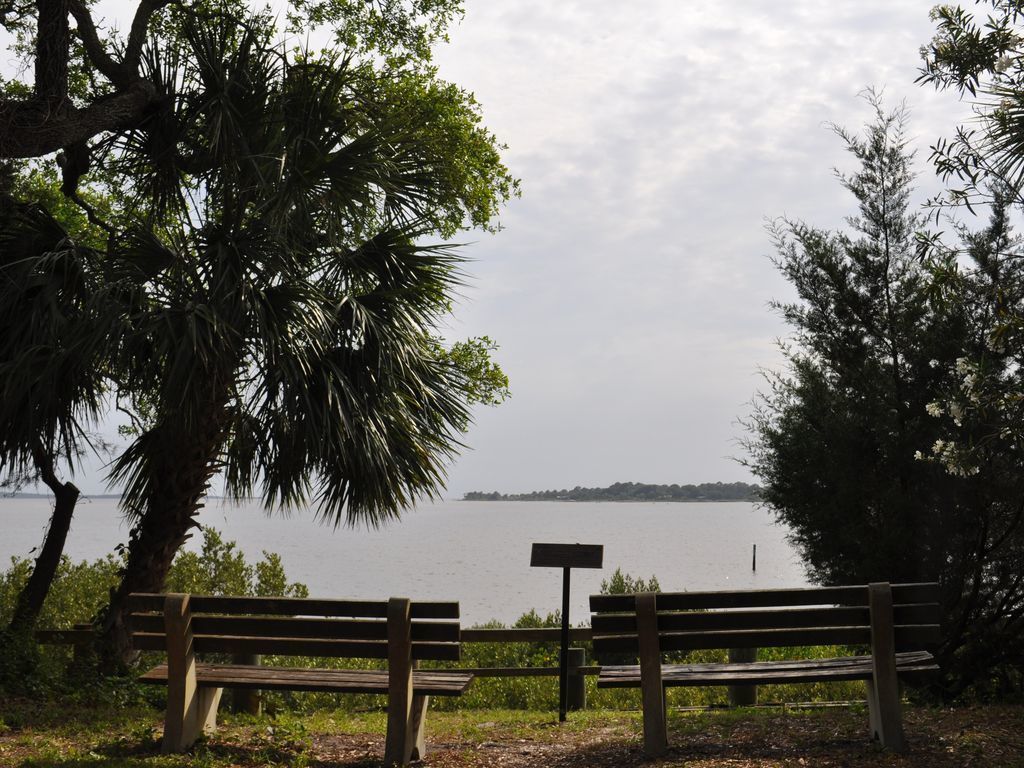 A bench and a sign in a park with a lake view.