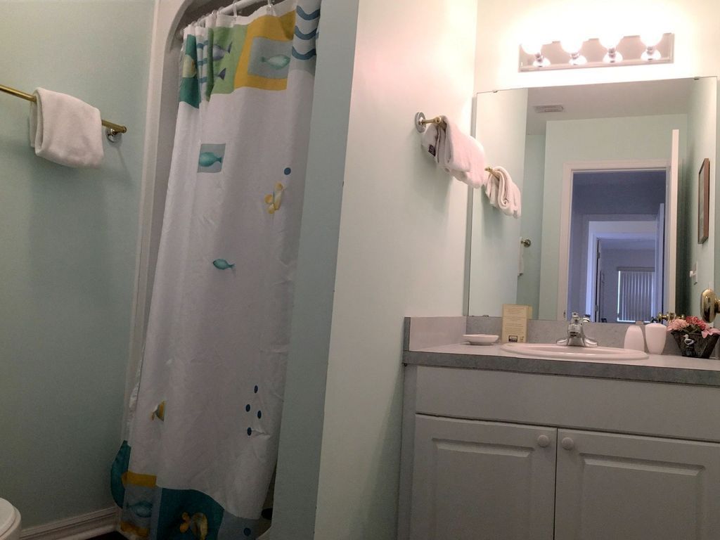 A bathroom with a shower curtain featuring fish patterns, a sink with a mirror above it, and towels hanging on the wall.