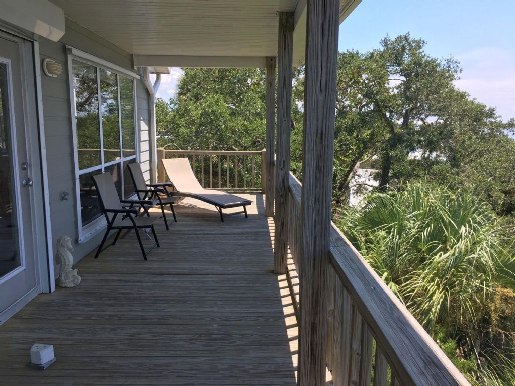 A wooden deck with lounge chairs and a stone statue, overlooking a lush landscape.