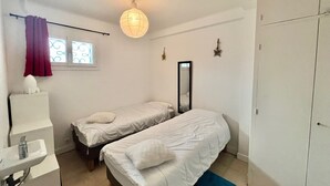 A small, well-lit bedroom with two single beds, a bedside table, a mirror, and a wardrobe. - 45 clemenceau (Cannes)