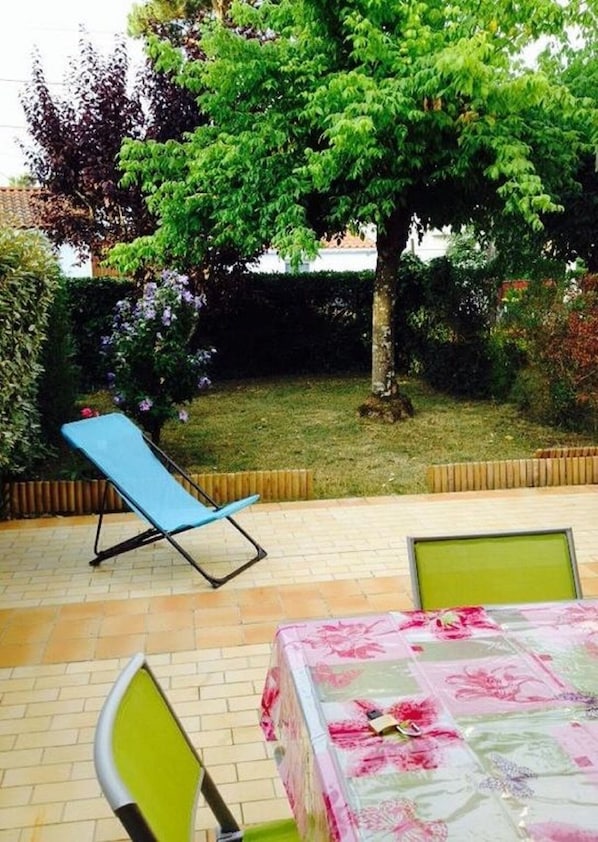A patio with a table covered in a floral tablecloth, a blue lounge chair, and a green chair.