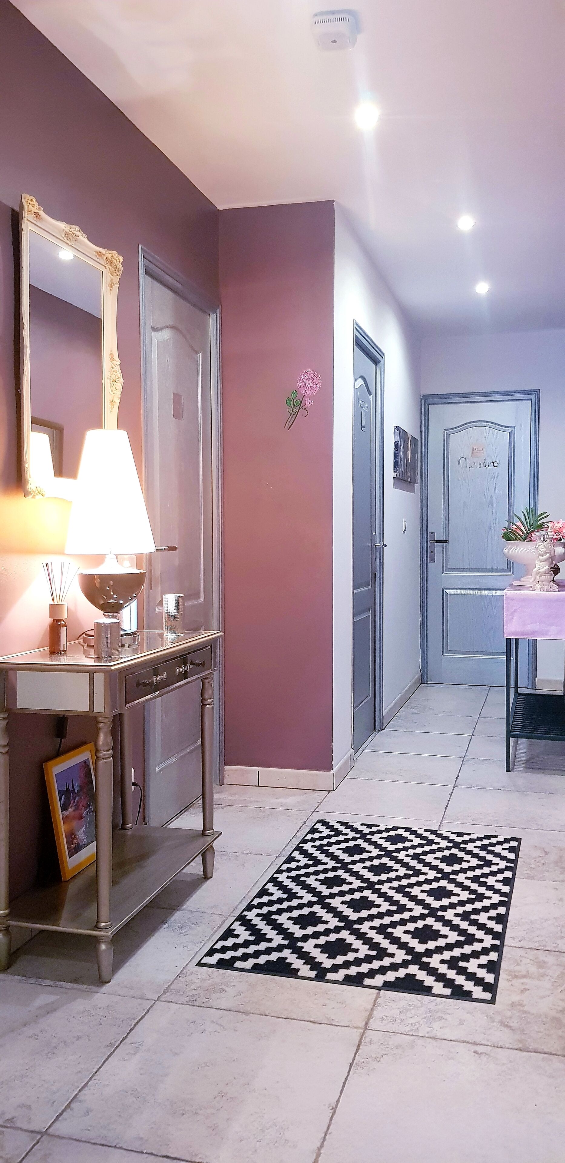 Un couloir avec une console, un miroir et une porte portant une plaque nominative.
