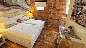 A modern bedroom with a brick wall, a large bed with white linens, a ceiling fan, and a small table with a plant. - Luxury Loft in Downtown Asheville: chic, central, in the middle of all the fun! (Asheville)