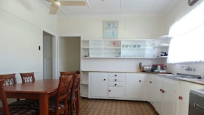 A compact kitchen with a dining table and chairs, white cabinets, and a patterned floor. - Sailor's Rest Holiday House (Lota)