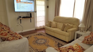 A living room with a beige sofa, patterned rug, and a flat-screen TV mounted on the wall. - Sailor's Rest Holiday House (Lota)