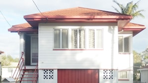 A single-story house with a red garage door, white siding, and a small front porch. - Sailor's Rest Holiday House (Lota)