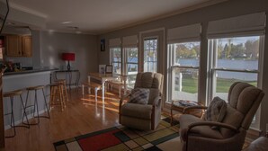Un vaste espace de vie avec vue sur un lac, un plancher en bois et une cuisine équipée d’un bar avec des tabourets.