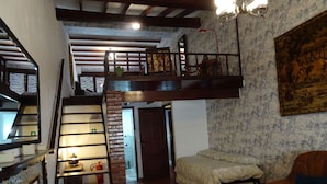 Habitación estilo loft con escalera de madera, cama, sofá y un cuadro en la pared.