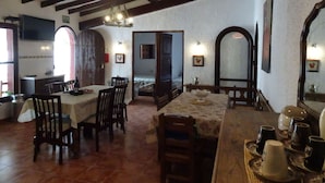 Un comedor con mesas y sillas de madera, una lámpara de araña y un televisor montado en la pared.