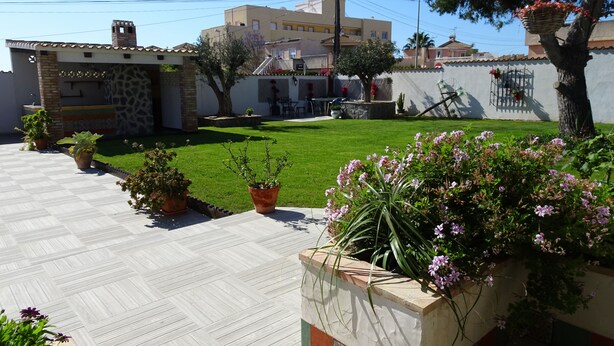 Un patio con suelo de baldosas, plantas en macetas y césped.