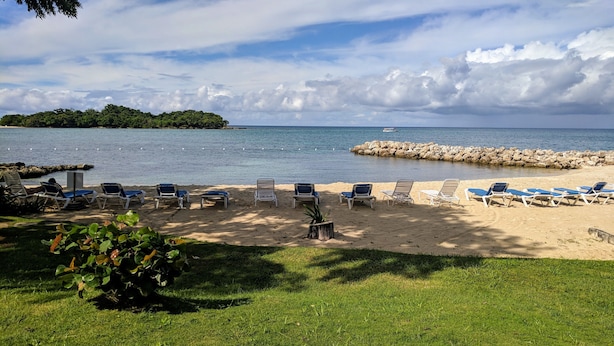 A beach with lounge chairs and a rocky breakwater. - Breezy Studio, footsteps from the beach.  (Negril)