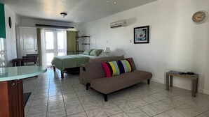 A spacious living area with a sofa, a dining table, and a kitchen in the background. - Breezy Studio, footsteps from the beach.  (Negril)