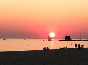 A sunset over a beach with boats and a few people on the shore.