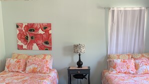 A room with two beds, each with floral bedding, a nightstand with a lamp, and a painting on the wall. - Charming House Located In Downtown Grand Haven (Grand Haven)