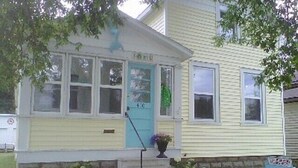 A two-story house with a front porch, a blue door, and a small garden with flowers. - Charming House Located In Downtown Grand Haven (Grand Haven)