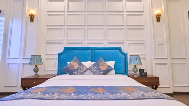Een slaapkamer met een blauw hoofdeinde, witte muren en een bed met een patroon.
