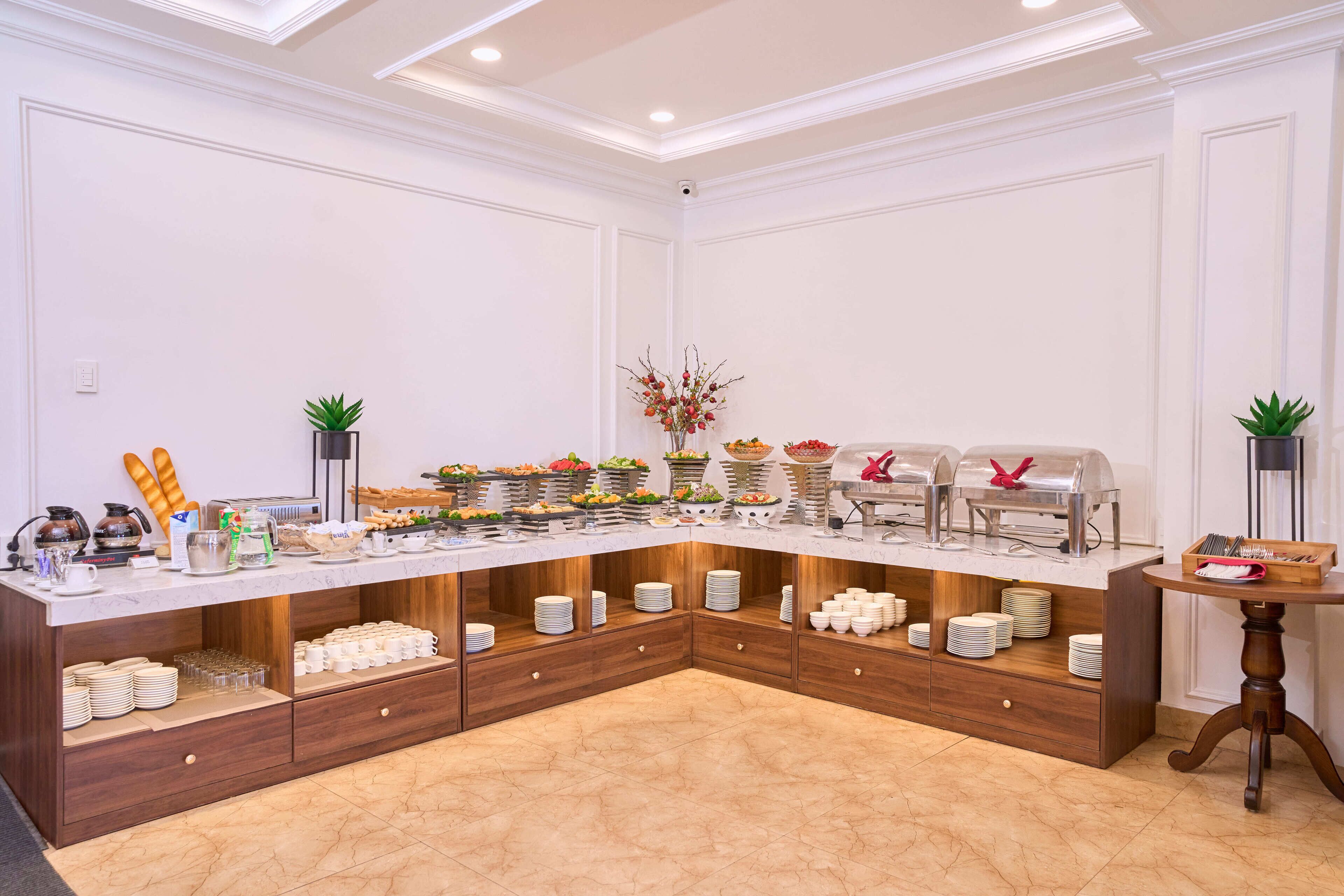 Ein reichhaltiges Buffet mit verschiedenen Speisen, Geschirr und einer Kaffeestation, ergänzt durch eine Zierpflanze.