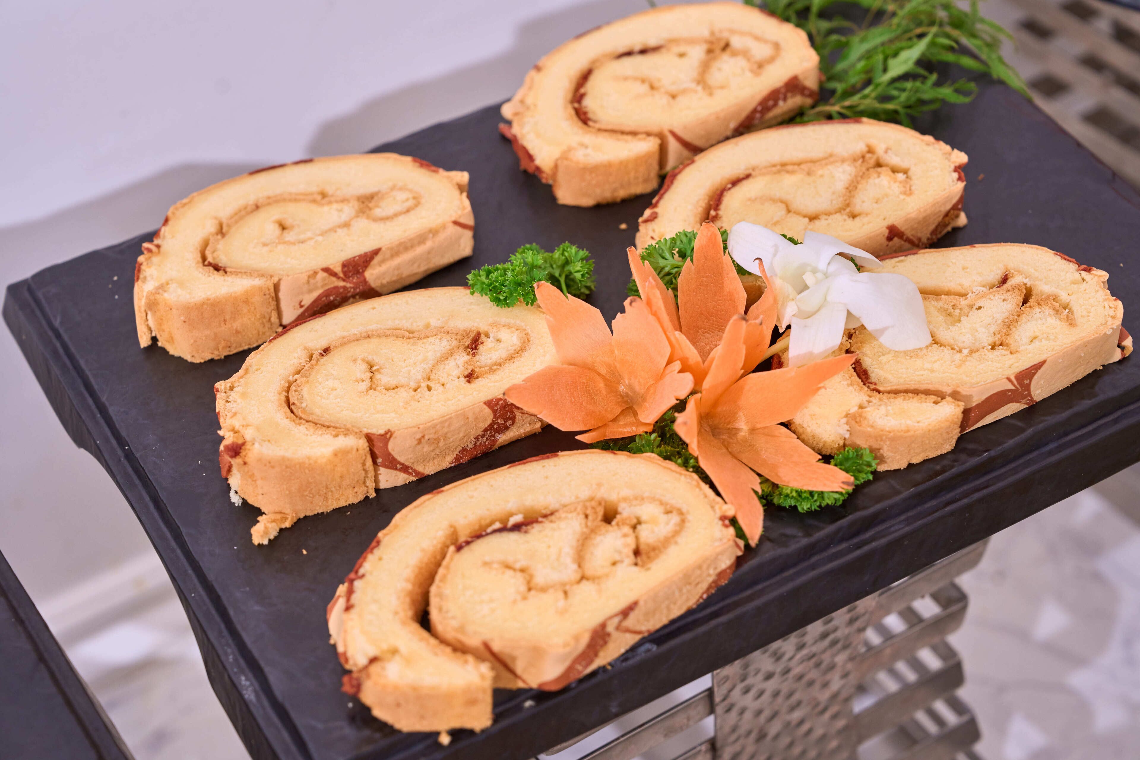 A tray of sliced rolls on a black plate, garnished with parsley and a white flower.
