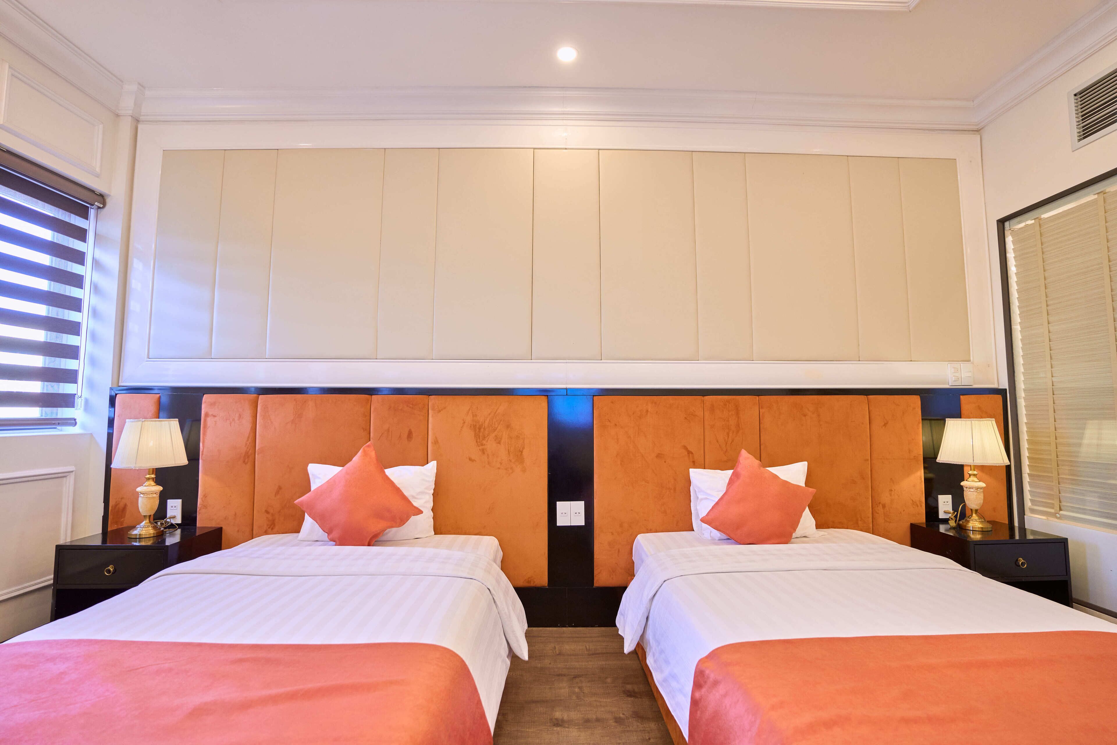Une chambre d’hôtel avec deux lits, une tête de lit en bois et une grande fenêtre avec des stores.