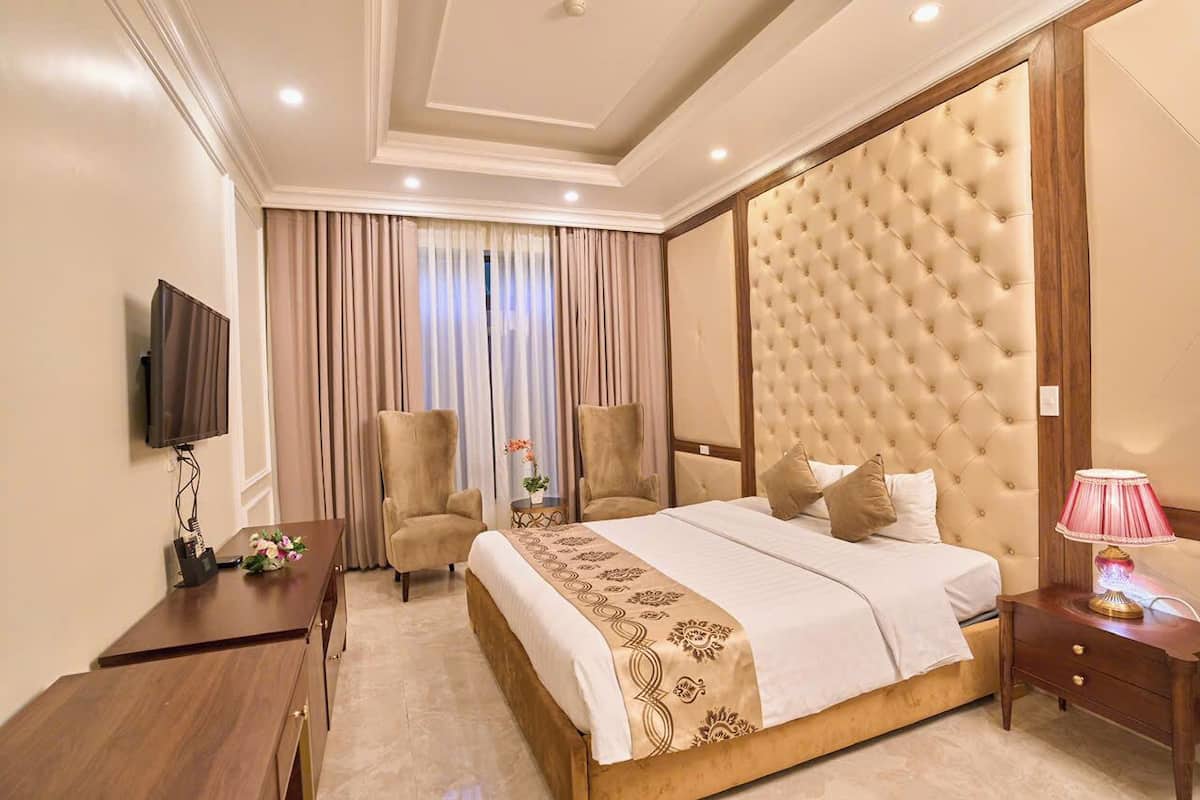 Een hotelkamer met een groot bed, twee fauteuils, een televisie en een nachtkastje met een lamp.