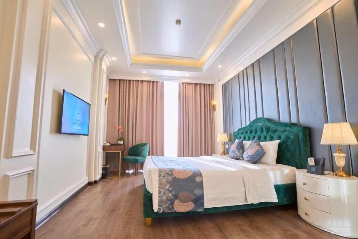 A hotel room with a large bed, a desk, a chair, and a television.