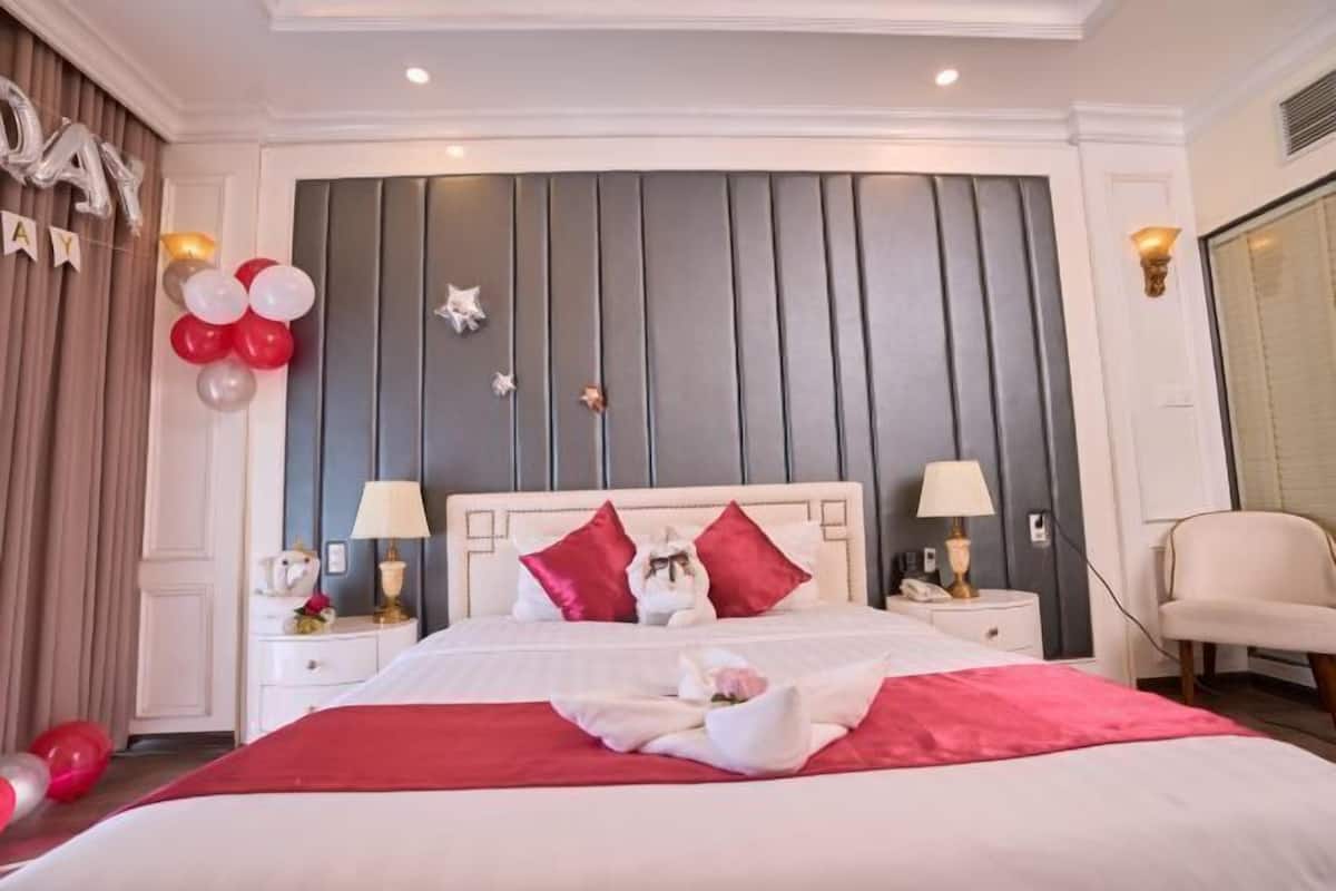 Een hotelkamer met een groot bed, twee nachtkastjes, een stoel en een wand met decoratieve details.