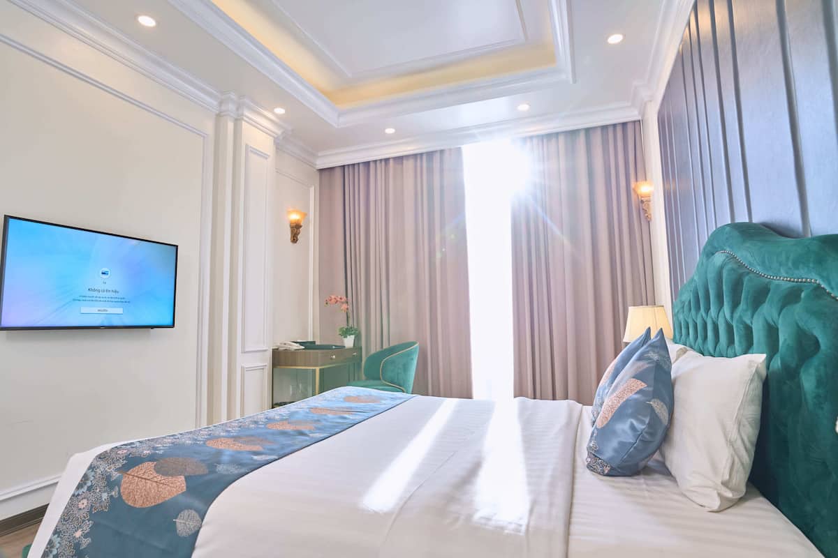 Een hotelkamer met een groot bed, een flatscreen televisie aan de muur, een bureau met stoel, en een raam met gordijnen.